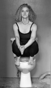Leslie Howard squats on top of a toilet seat in yoga clothes