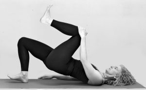 Leslie Howard does a one-legged bridge pose holding one knee to awaken the glutes